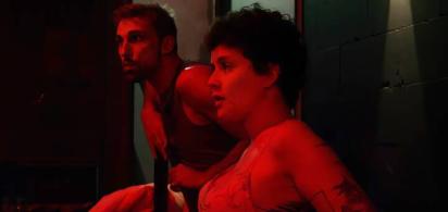 Szenenfotoeine zwei Personen im sitzen nebeneinander in einem rot beleuchteten Raum